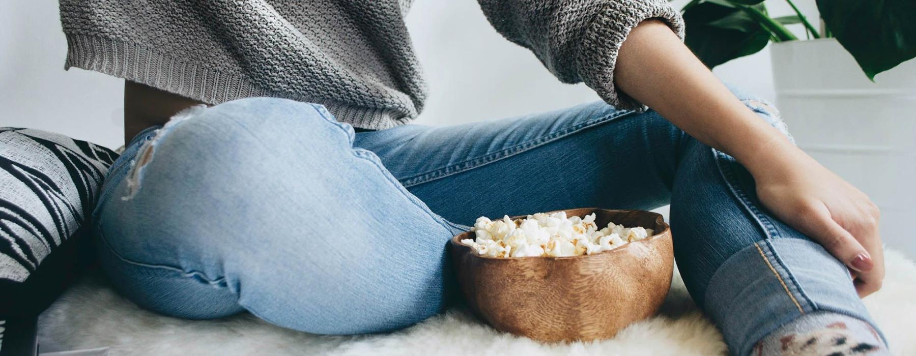 woman sits on a rug with a bowl of popcorn